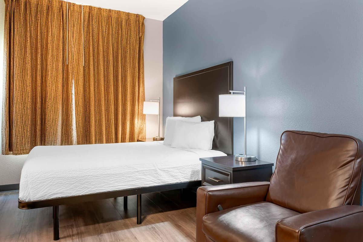 Una camera d'albergo con un letto, una sedia, un comodino e una lampada.