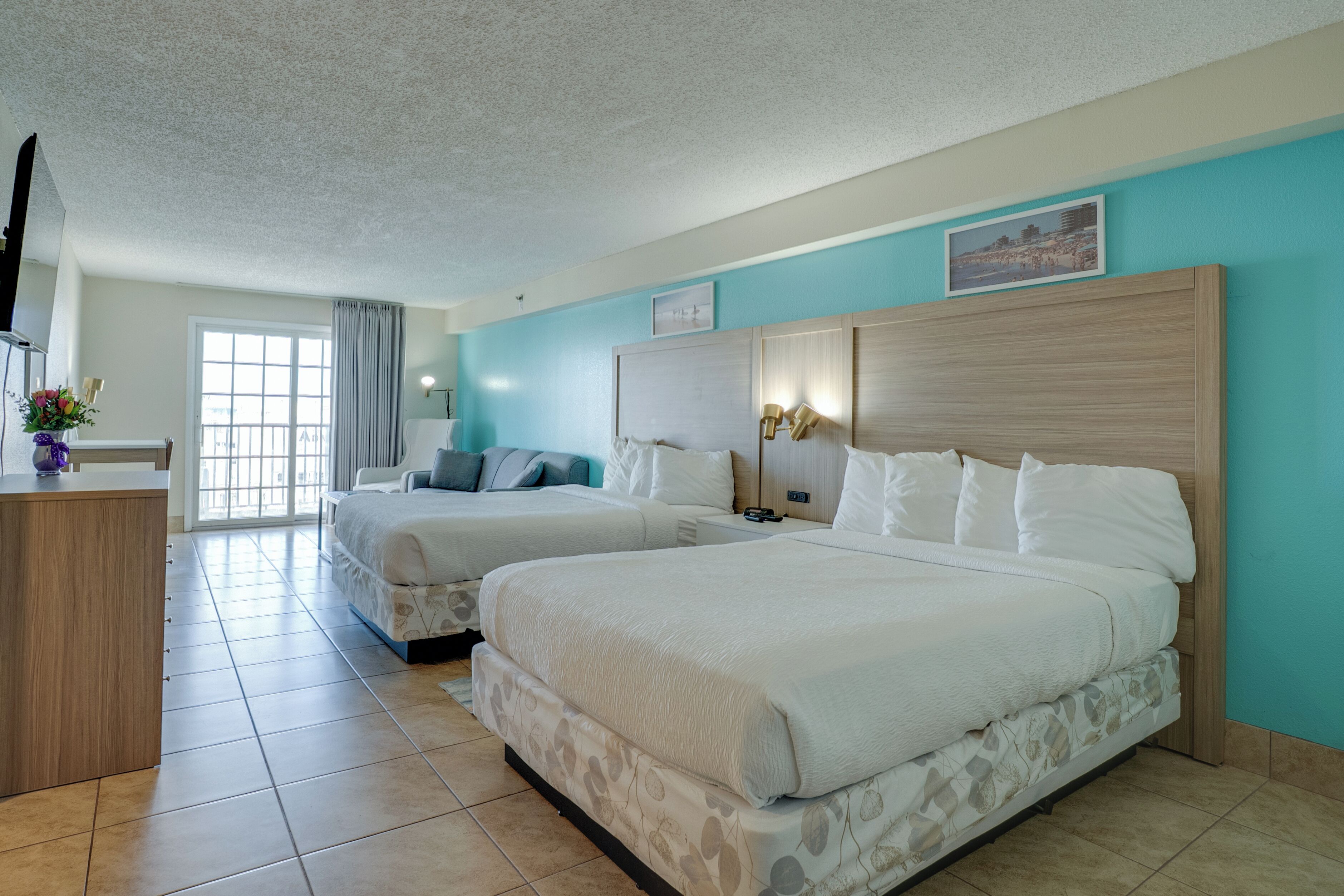 A hotel room with two beds, a desk, and a window with curtains.