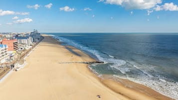 A beach with a long stretch of sand, a rocky breakwater, and buildings along the coastline.
