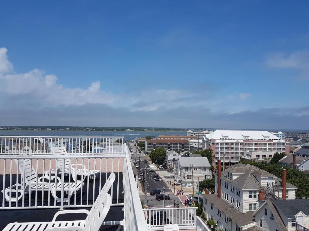 A coastal cityscape with a view of the sea, buildings, and a white fence with white chairs.