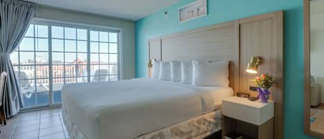 Quarto de hotel com uma cama grande, uma mesa de cabeceira com abajur, um criado-mudo pequeno e uma janela com vista para edifícios.