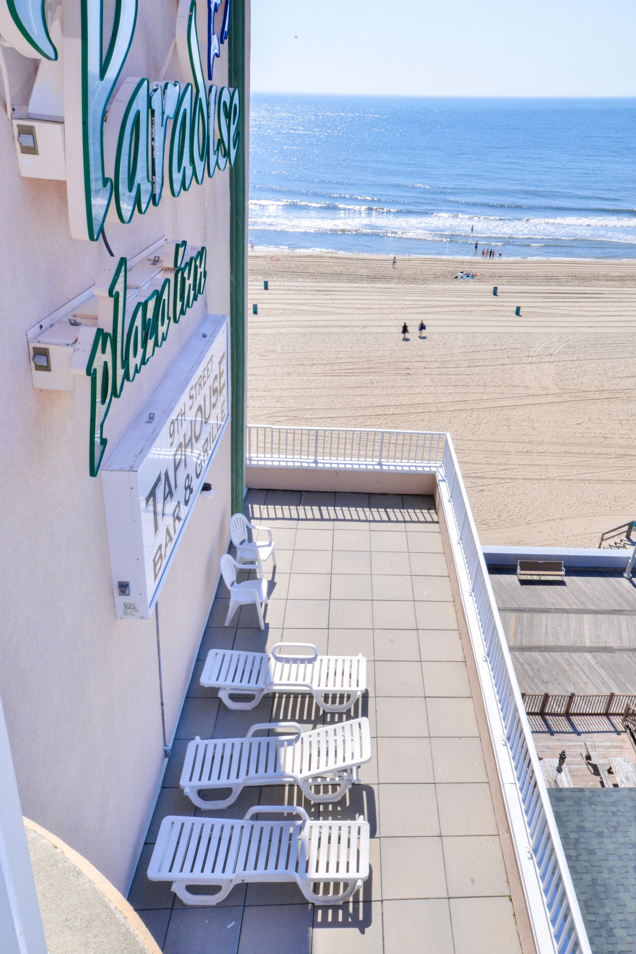 Una terraza frente al mar con sillas reclinables blancas y un letrero que dice 'Paradise Tropical Bar & Grill'.