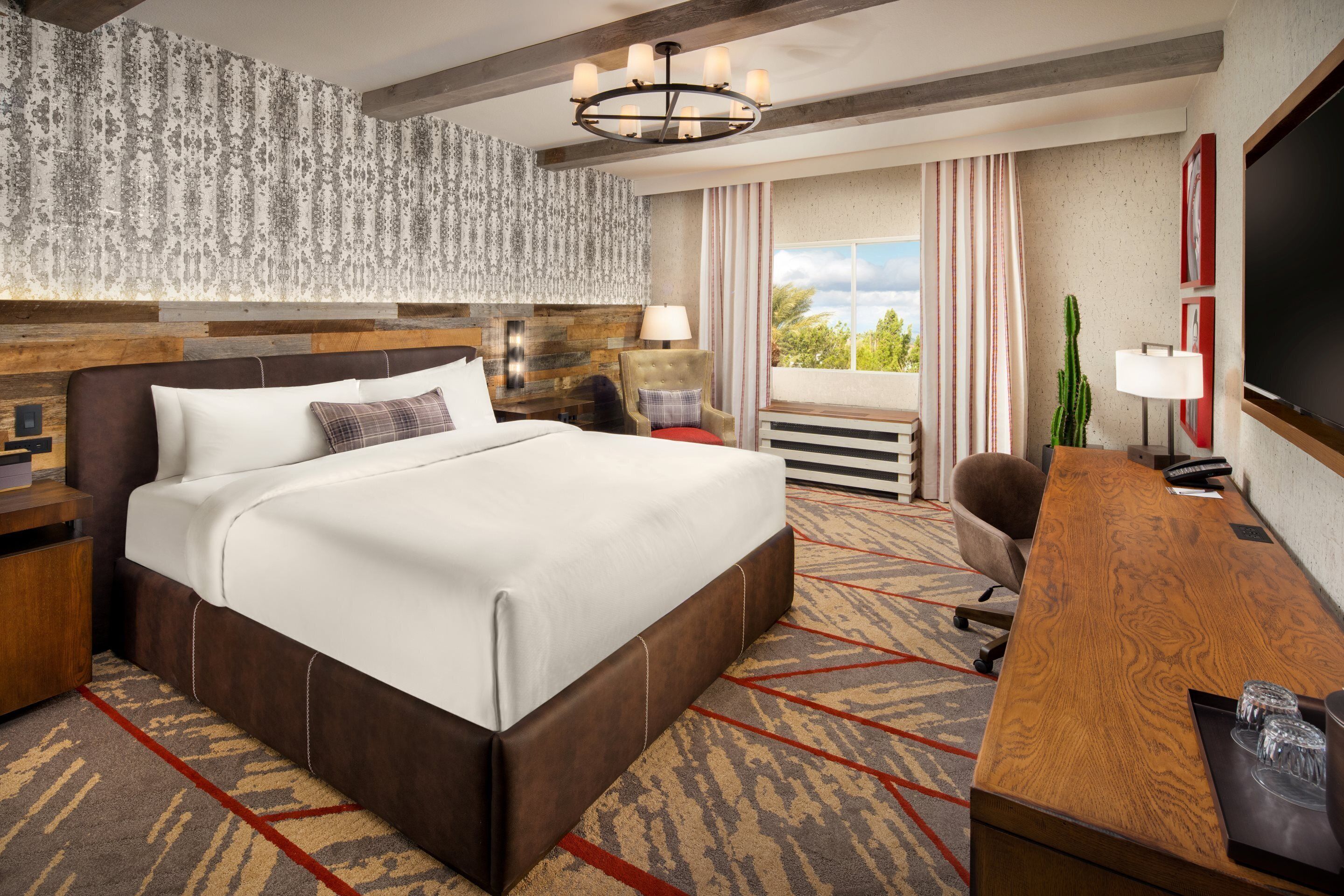 Een hotelkamer met een groot bed, een houten bureau, een televisie en uitzicht op de omgeving.