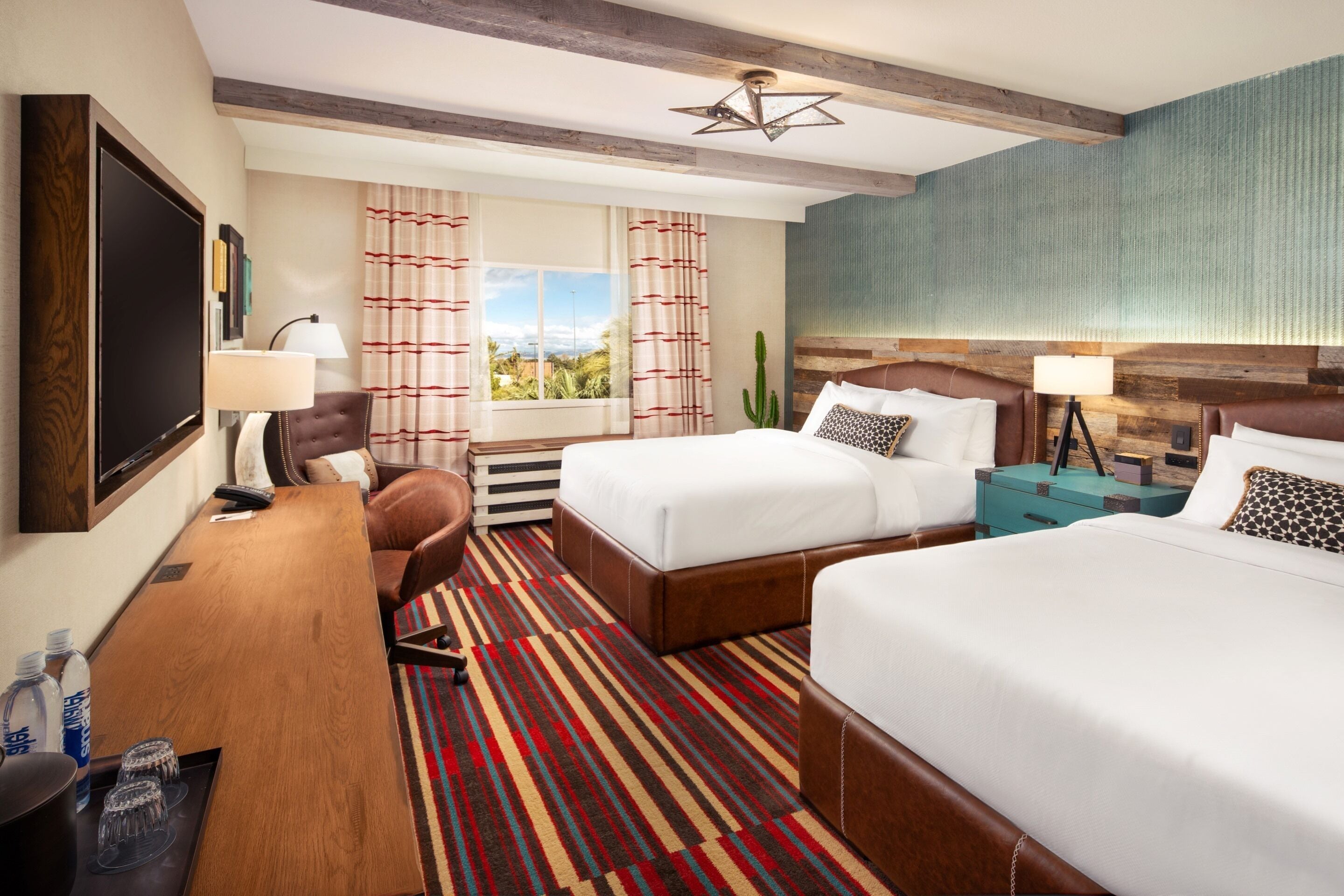 A hotel room with two beds, a desk with a chair, a TV, and a window with curtains.