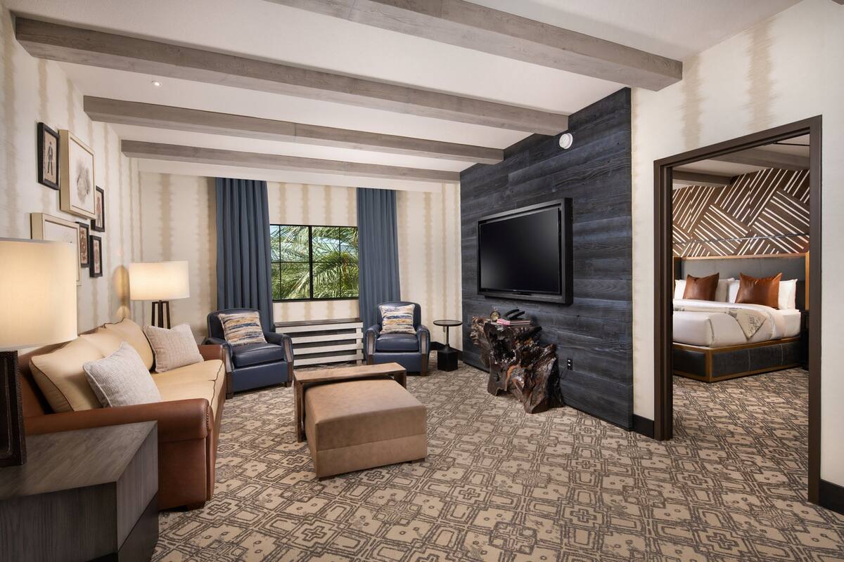 Een moderne hotelkamer met een grote flatscreen-tv, een bank, een bijzettafeltje en een kamerbreed tapijt met een patroon.