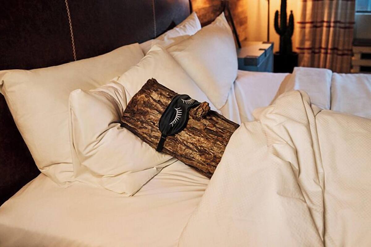 Een bed met witte lakens, een houten kussen en een zwarte muts.