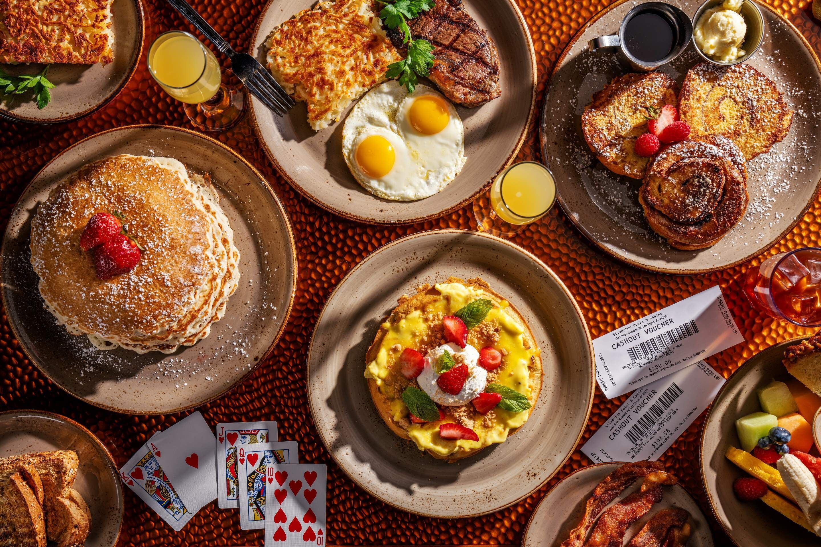 A breakfast spread with pancakes, eggs, bacon, and fruit.