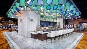 Un espace bar au design moderne, avec un comptoir central doté de tabourets et un grand plafond illuminé agrémenté de miroirs circulaires.