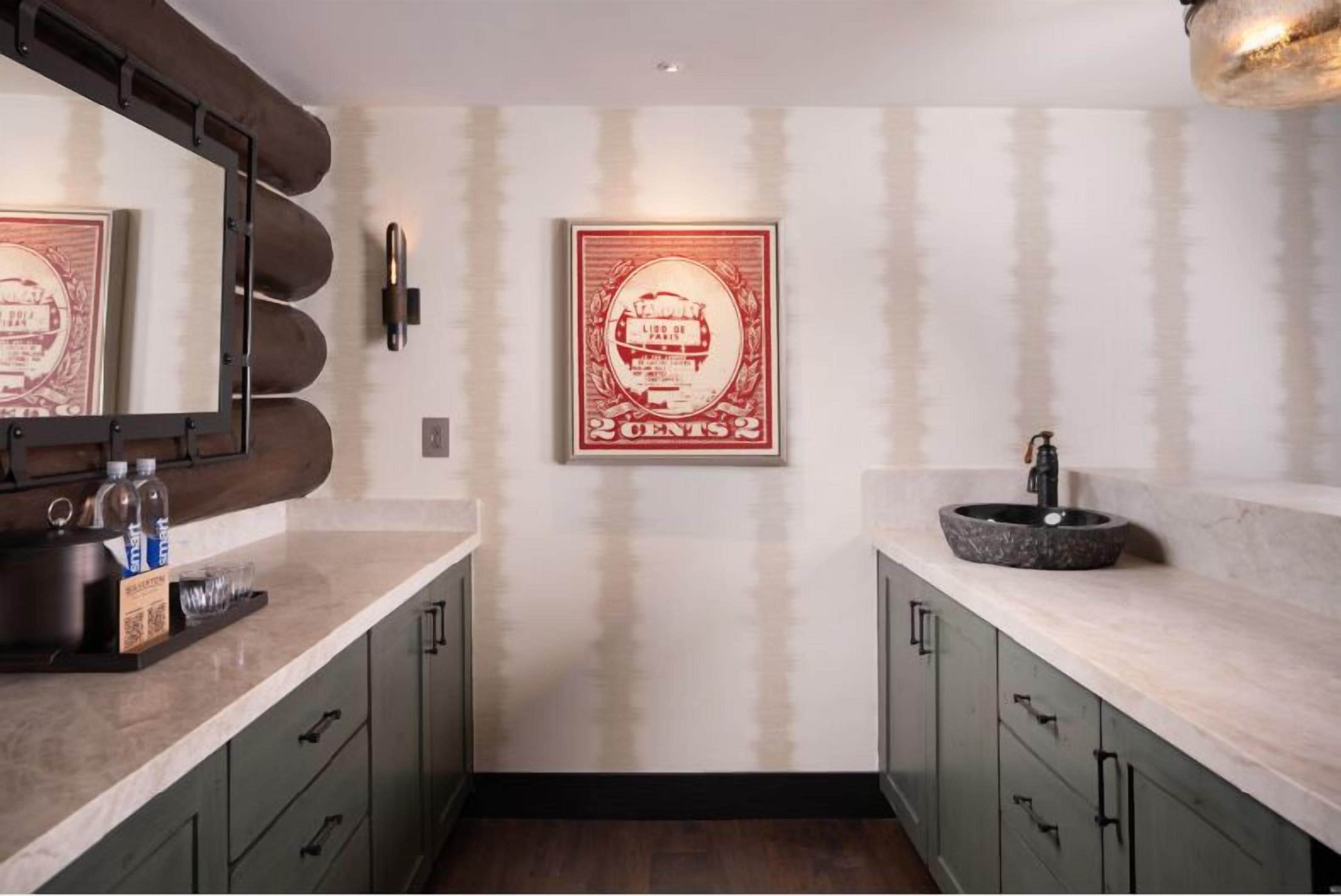A bathroom with a marble sink, a large mirror, and a framed vintage poster on the wall.