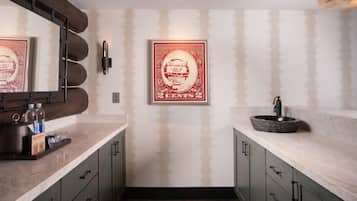 A bathroom with a marble sink, a large mirror, and a framed vintage poster on the wall.