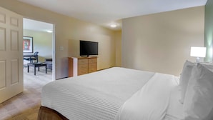 A hotel room with a large bed, a television on a stand, a desk with a chair, and a door leading to another room. - Extended Stay America Select Suites Raleigh RTP 4610 Miami B (Durham)