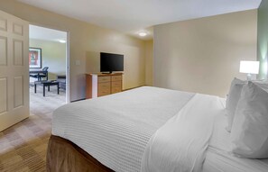 Ein Hotelzimmer mit einem großen Bett, einem Fernseher auf einem Schrank, einem Schreibtisch mit Stuhl und einer Tür zu einem anderen Raum.