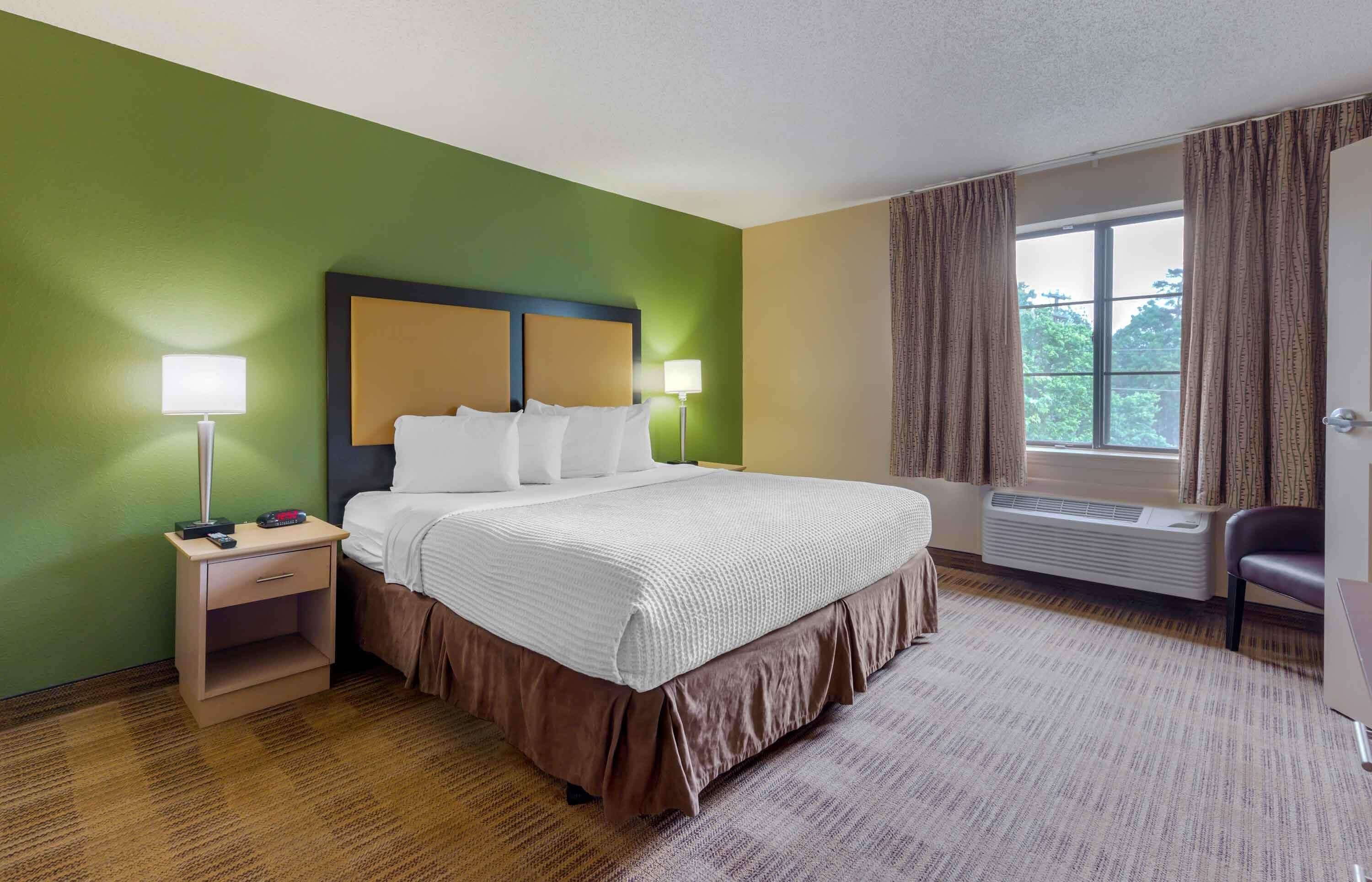 Een hotelkamer met een bed, nachtkastjes, een raam met gordijnen en een radiator.
