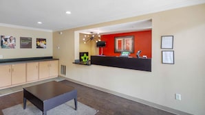 A reception area with a counter, a seating area, and a wall with informational posters. - Extended Stay America Select Suites Raleigh RTP 4610 Miami B (Durham)