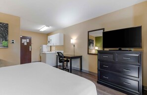 A hotel room with a large bed, a desk with a chair, a flat-screen TV, a dresser, and a microwave in the kitchenette. - Extended Stay America Select Suites Raleigh RTP 4610 Miami B (Durham)