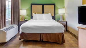 A hotel room with a bed, two bedside lamps, a television, and a heater. - Extended Stay America Select Suites Raleigh RTP 4610 Miami B (Durham)