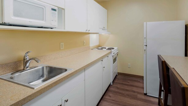 A kitchen with white cabinets, a stainless steel sink, a microwave, a stove, and a refrigerator. - Extended Stay America Select Suites Raleigh RTP 4610 Miami B (Durham)