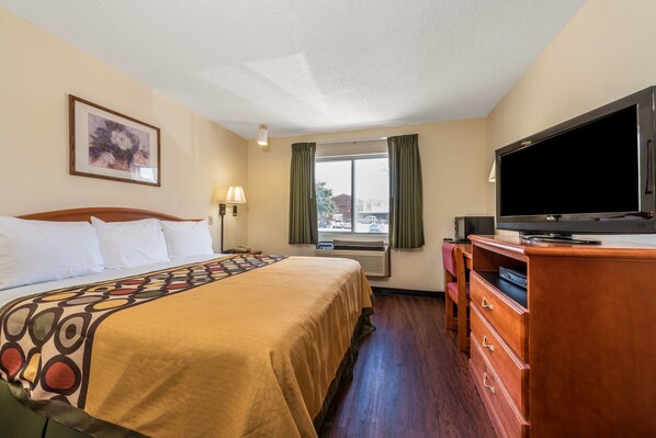 Una habitación de hotel con una cama, televisión, cómoda, ventana con cortinas y un cuadro en la pared.