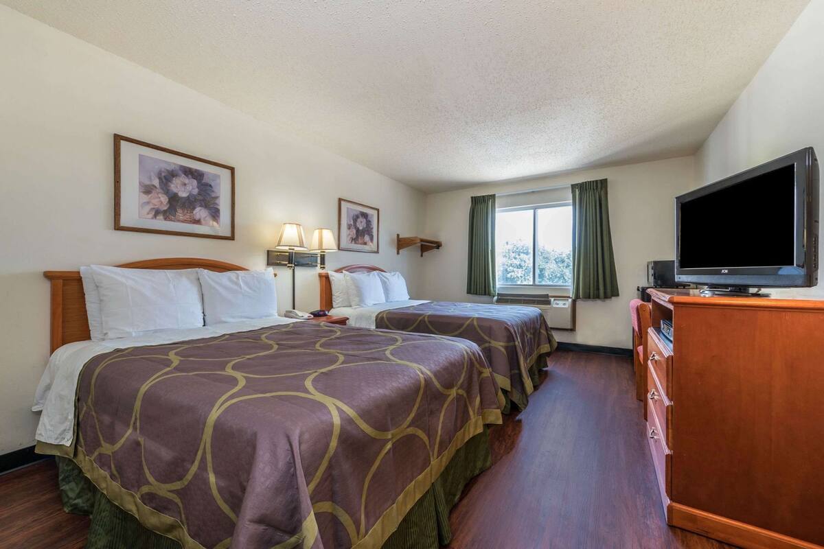 Ein Hotelzimmer mit zwei Betten, einem Fernseher, einem Schminktisch und einem Fenster mit Vorhängen.