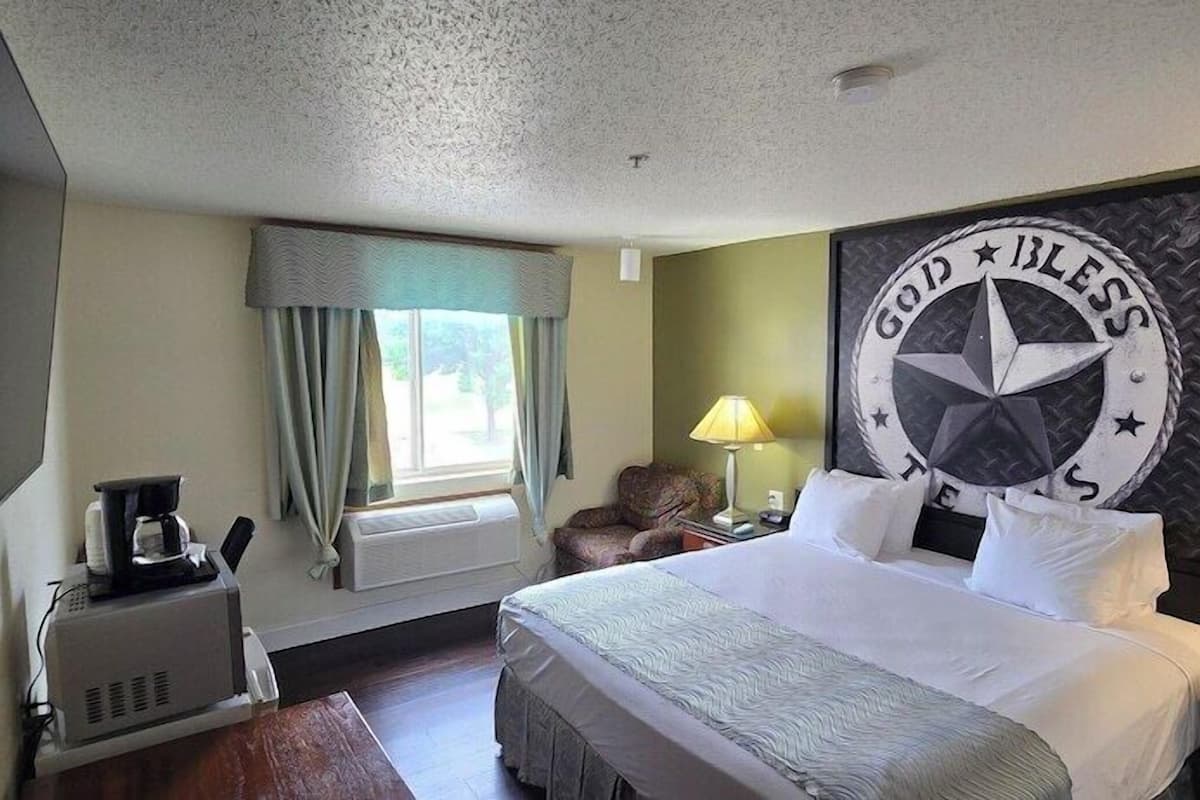 Ein Hotelzimmer mit einem Bett, einem Schreibtisch mit Kaffeemaschine, einer Lampe, einem Fernseher und einer Wand mit Kompassmuster.