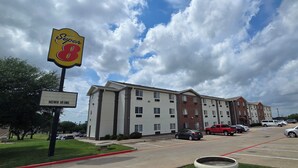 Ein Super 8 Hotel mit Parkplatz, Grünfläche und einem teilweise bewölkten Himmel.