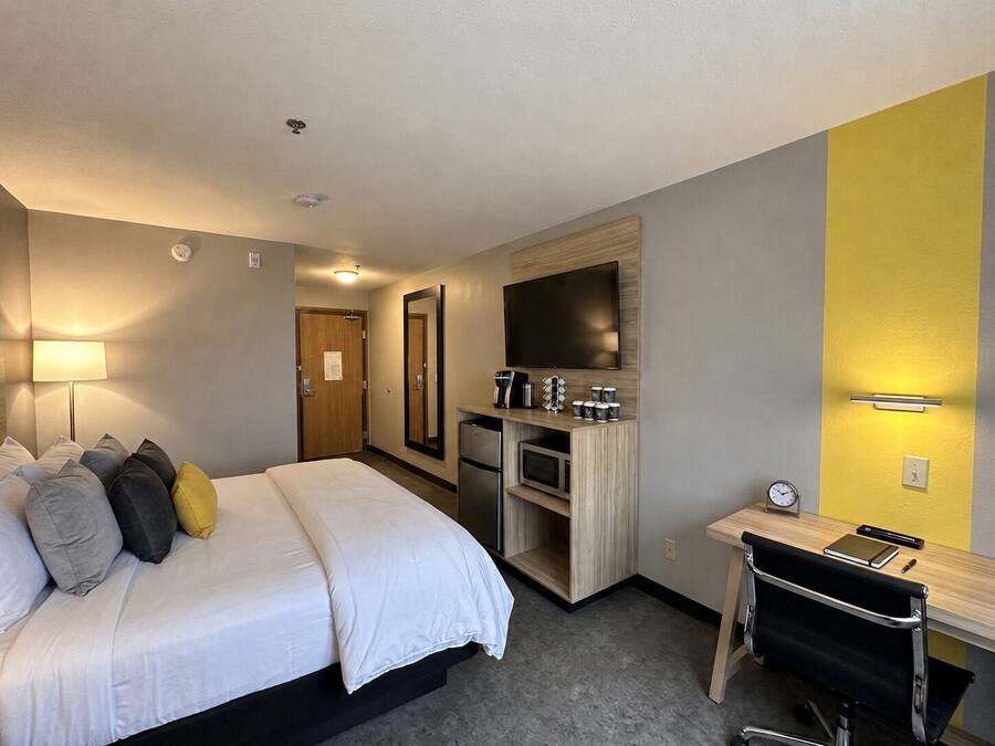 Quarto de hotel com cama, escrivaninha, espelho, televisão e micro-ondas.