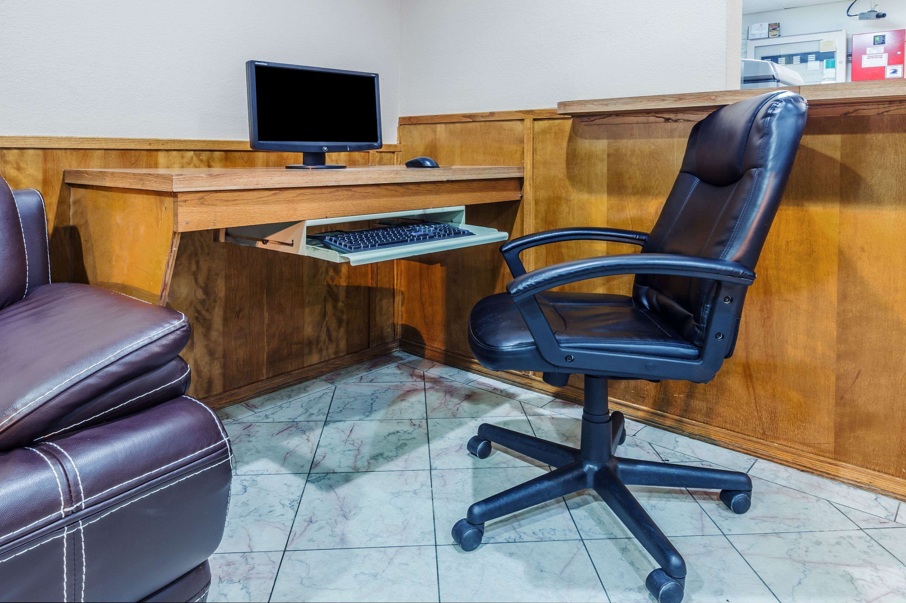 Een houten bureau met een computer monitor, toetsenbord en een zwarte kantoorstoel.
