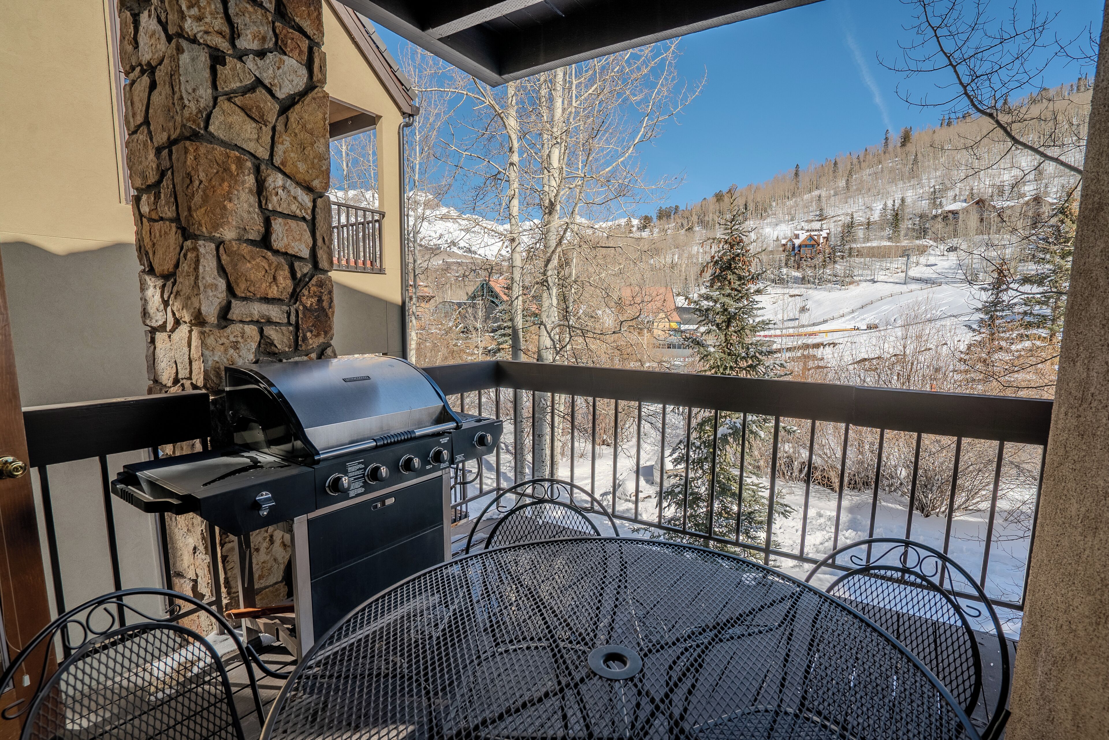 A balcony with a stone wall, a grill, and a metal table.