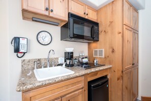 A kitchen with wooden cabinets, a microwave, a coffee maker, and a sink.