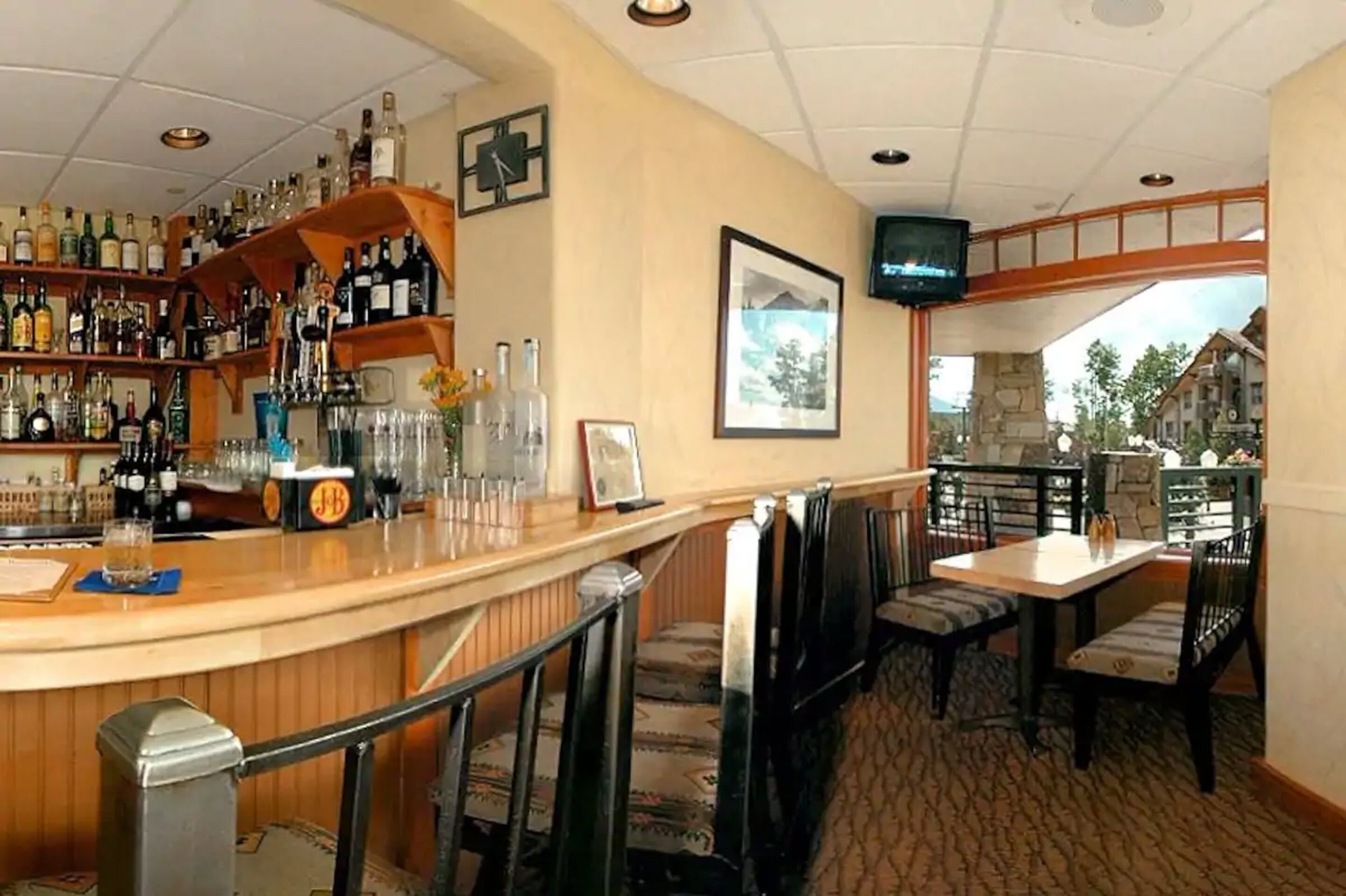 A bar area with a wooden counter, shelves of liquor bottles, and a television mounted on the wall.