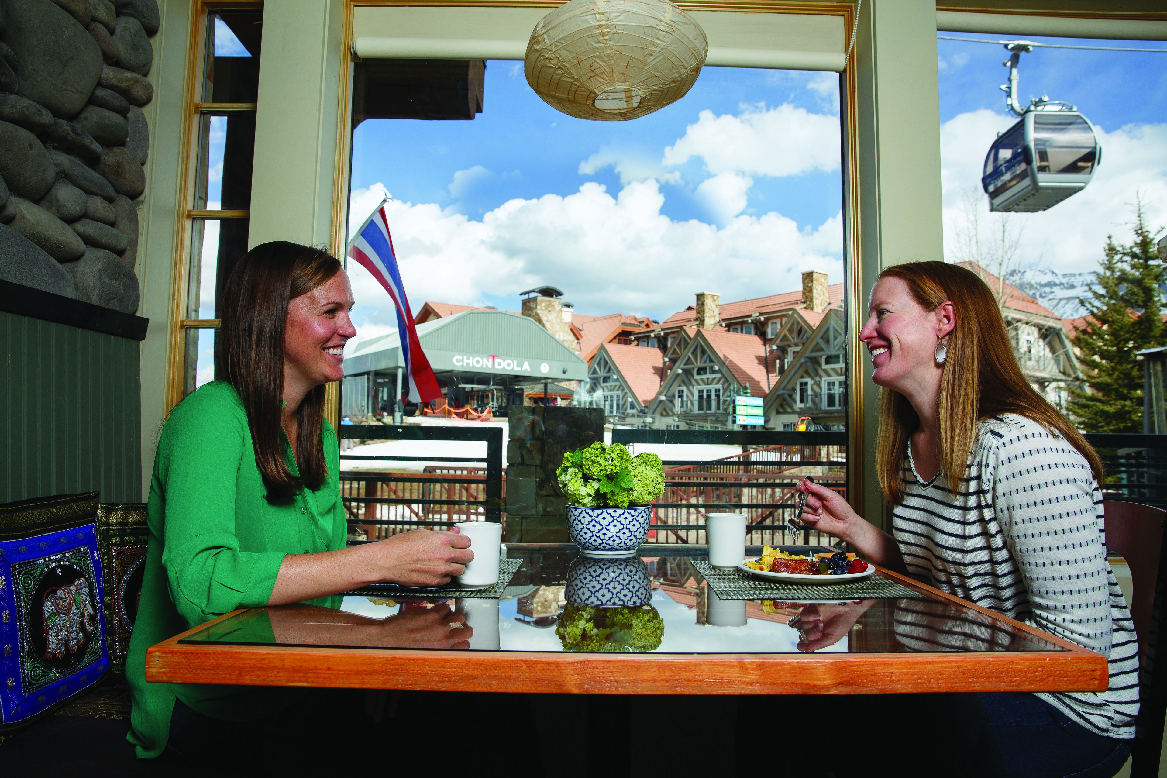 Two people seated at a table with a view of a building labeled "CHONDOLA" and a flag.