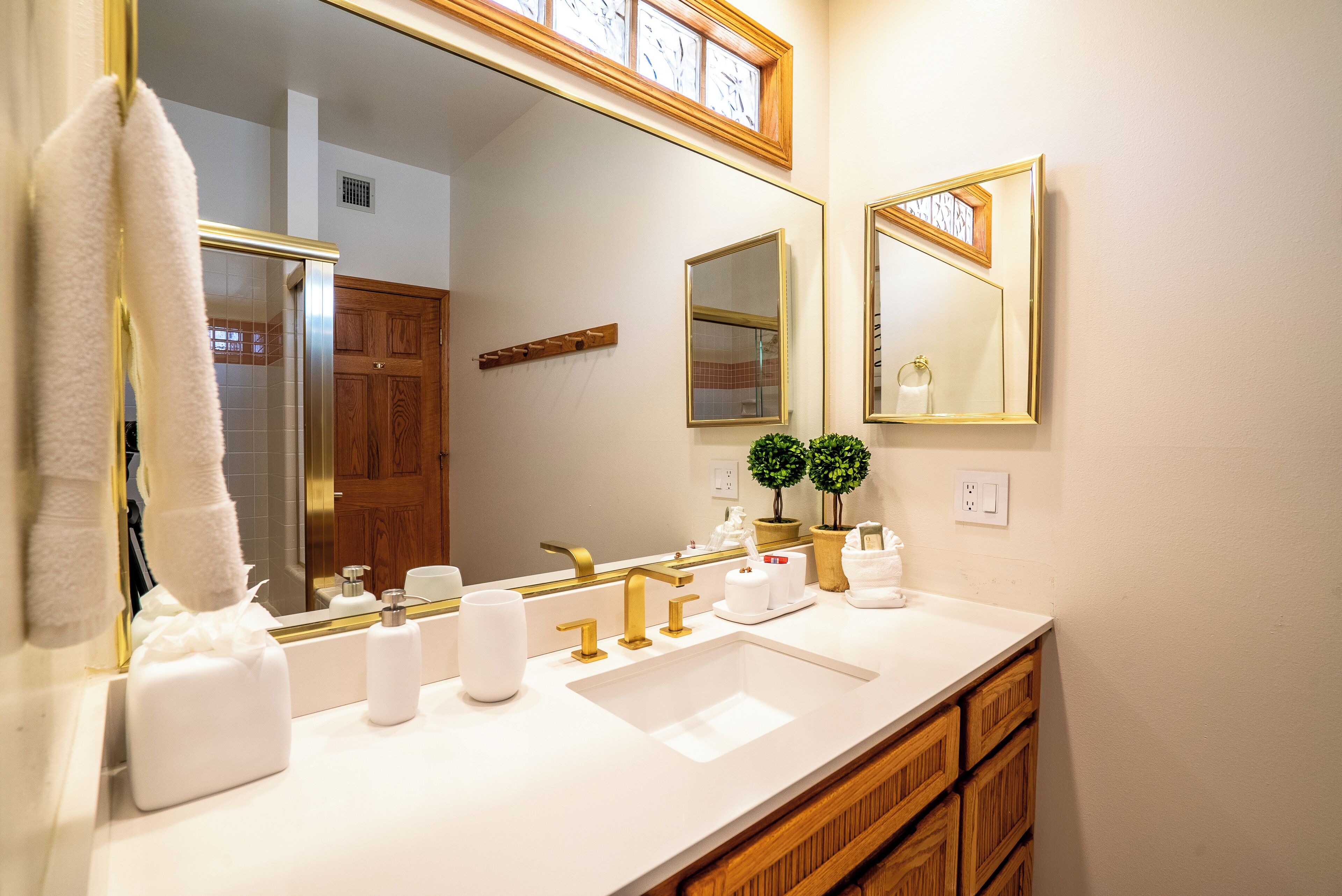 A bathroom with a white sink, gold faucets, a large mirror, and wooden cabinets.