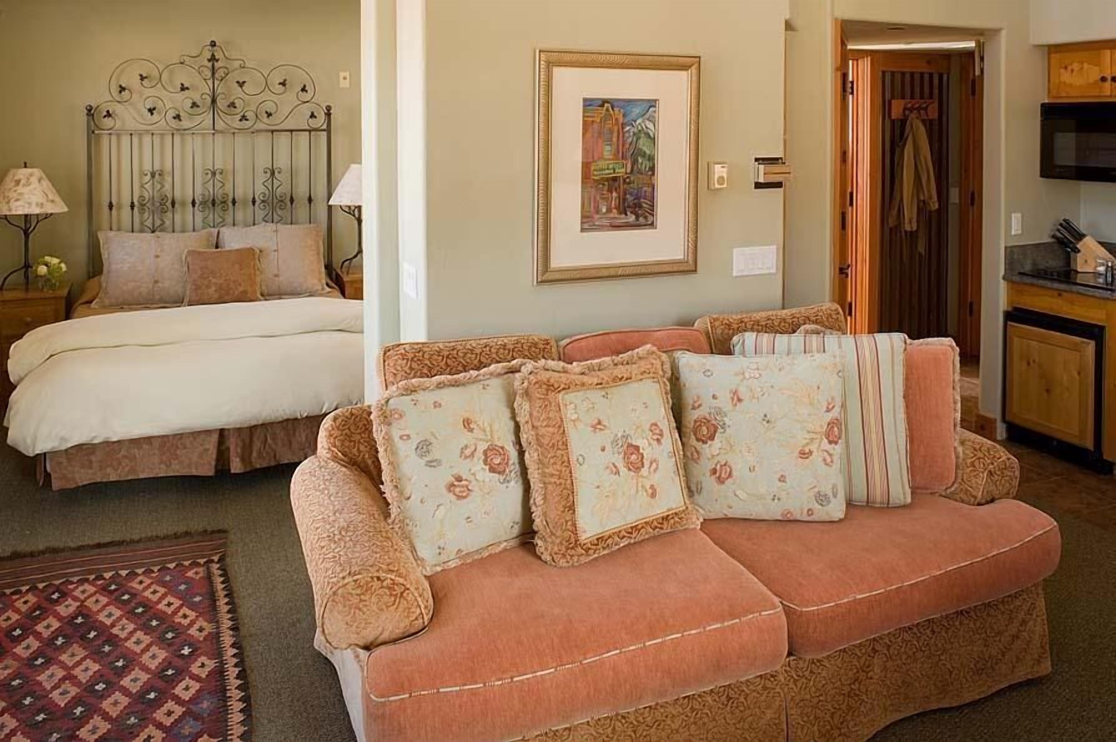 A cozy room with a bed, a sofa, a framed picture on the wall, and a kitchen area.