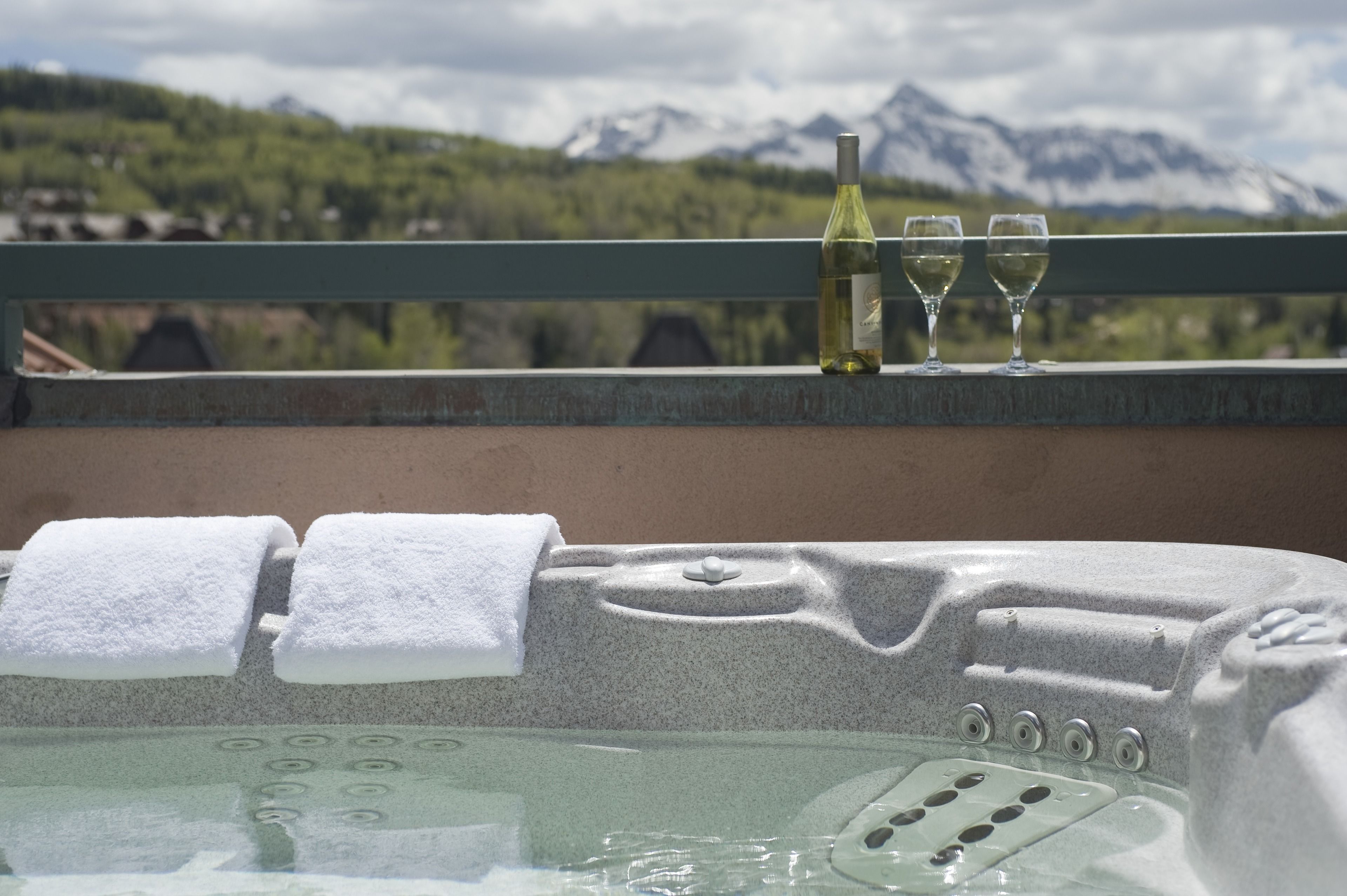 A hot tub with two towels and two wine glasses on a balcony with a mountain view.
