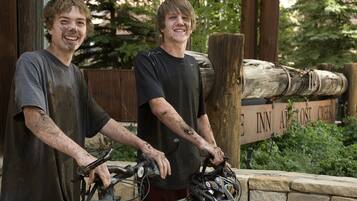 Dos personas de pie junto a bicicletas, con un letrero de madera al fondo.