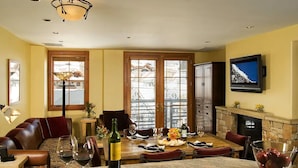 Un comedor con una mesa de madera dispuesta para una comida, una chimenea y un televisor montado en la pared.