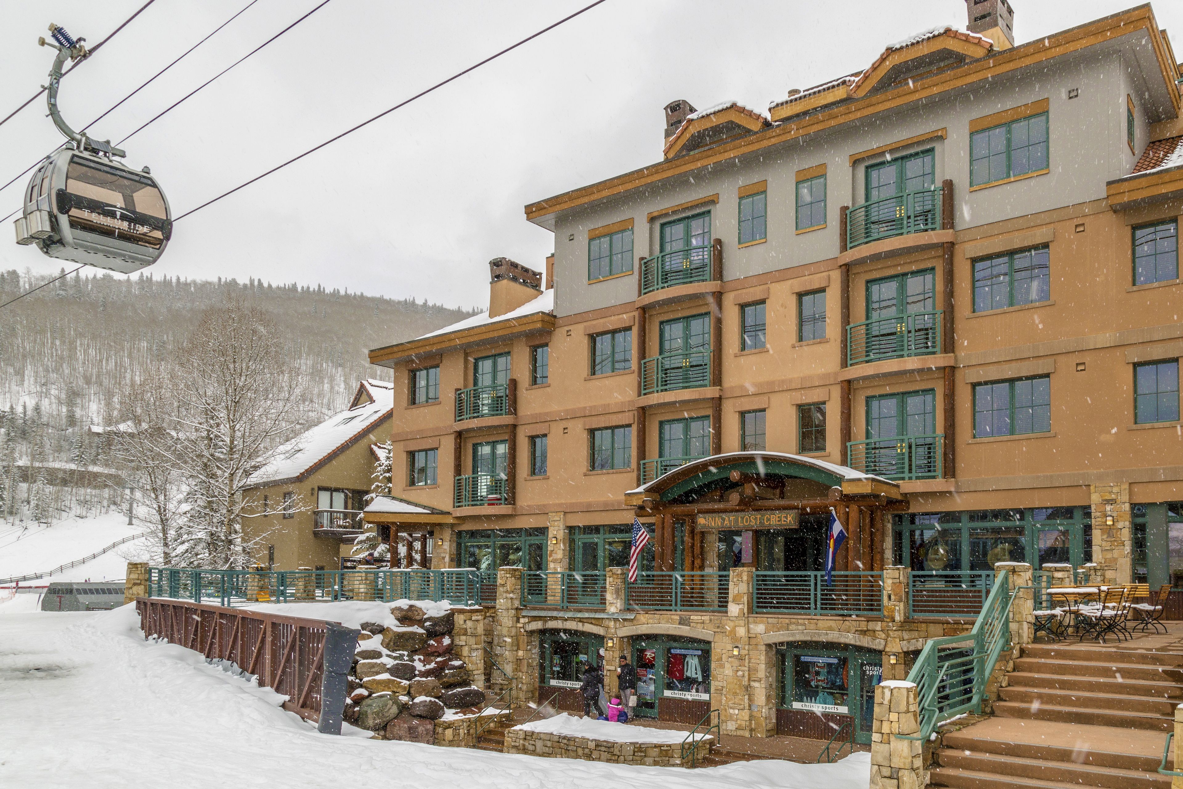 Un hotel de varios pisos con un telesilla, fachada de piedra y zona de estar al aire libre.