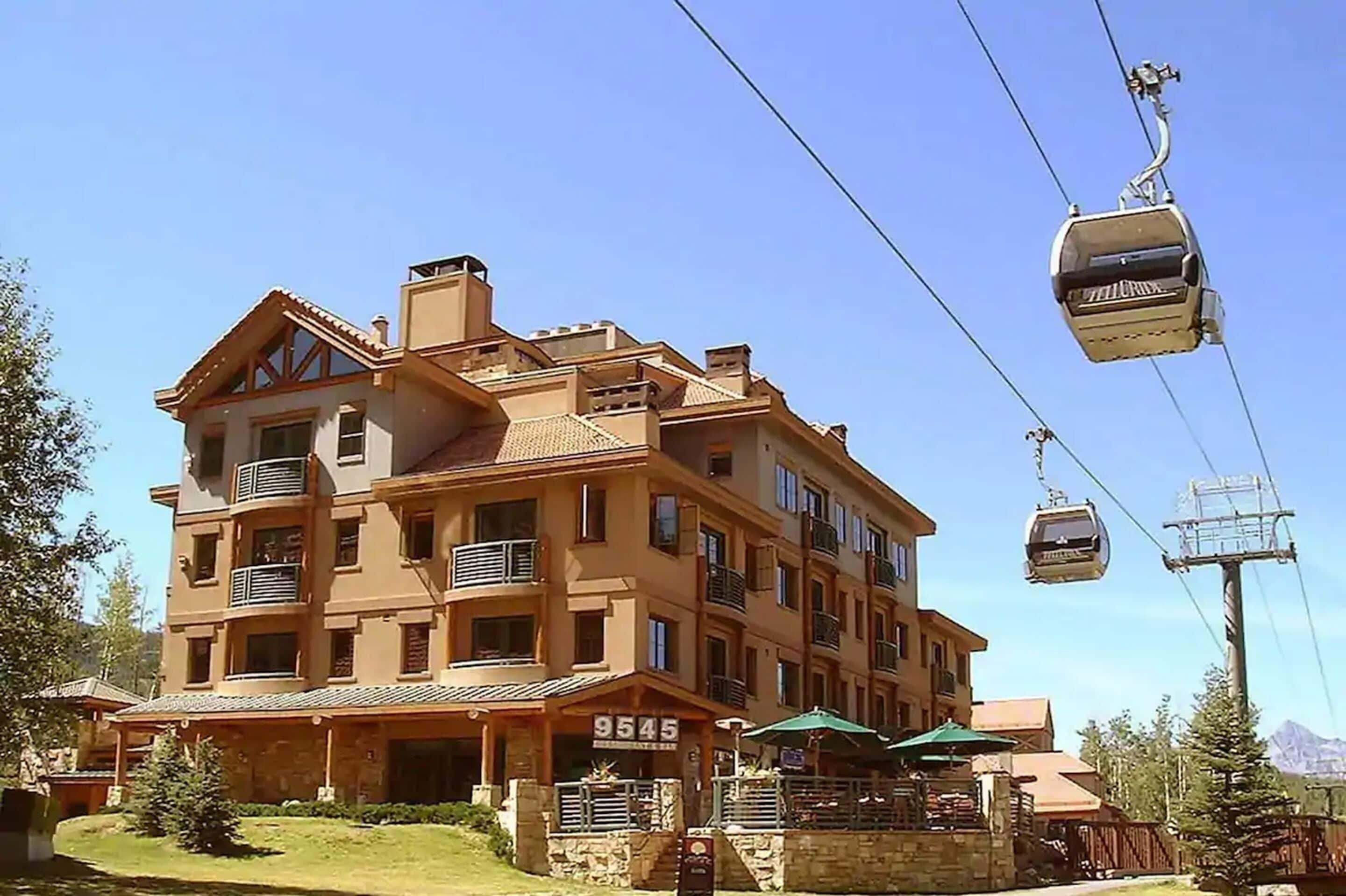 A multi-story hotel with a stone facade, balconies, and a ski lift in operation.