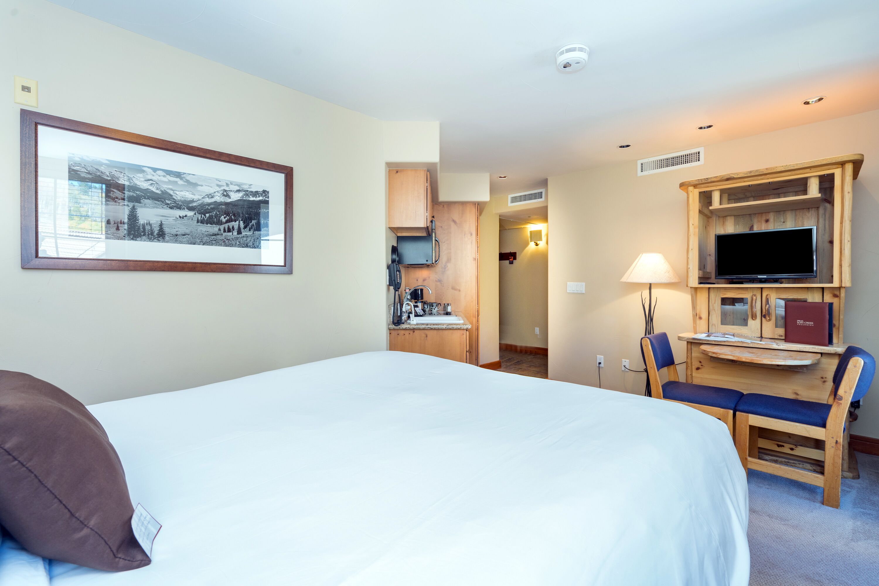 A hotel room with a large bed, a desk with a chair, a television, and a framed picture on the wall.
