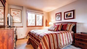 Un dormitorio con una cama grande, un aparador de madera, un televisor y dos cuadros en la pared.