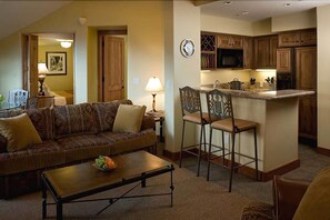 A living room with a sofa, coffee table, and a kitchen area with wooden cabinets and a microwave.