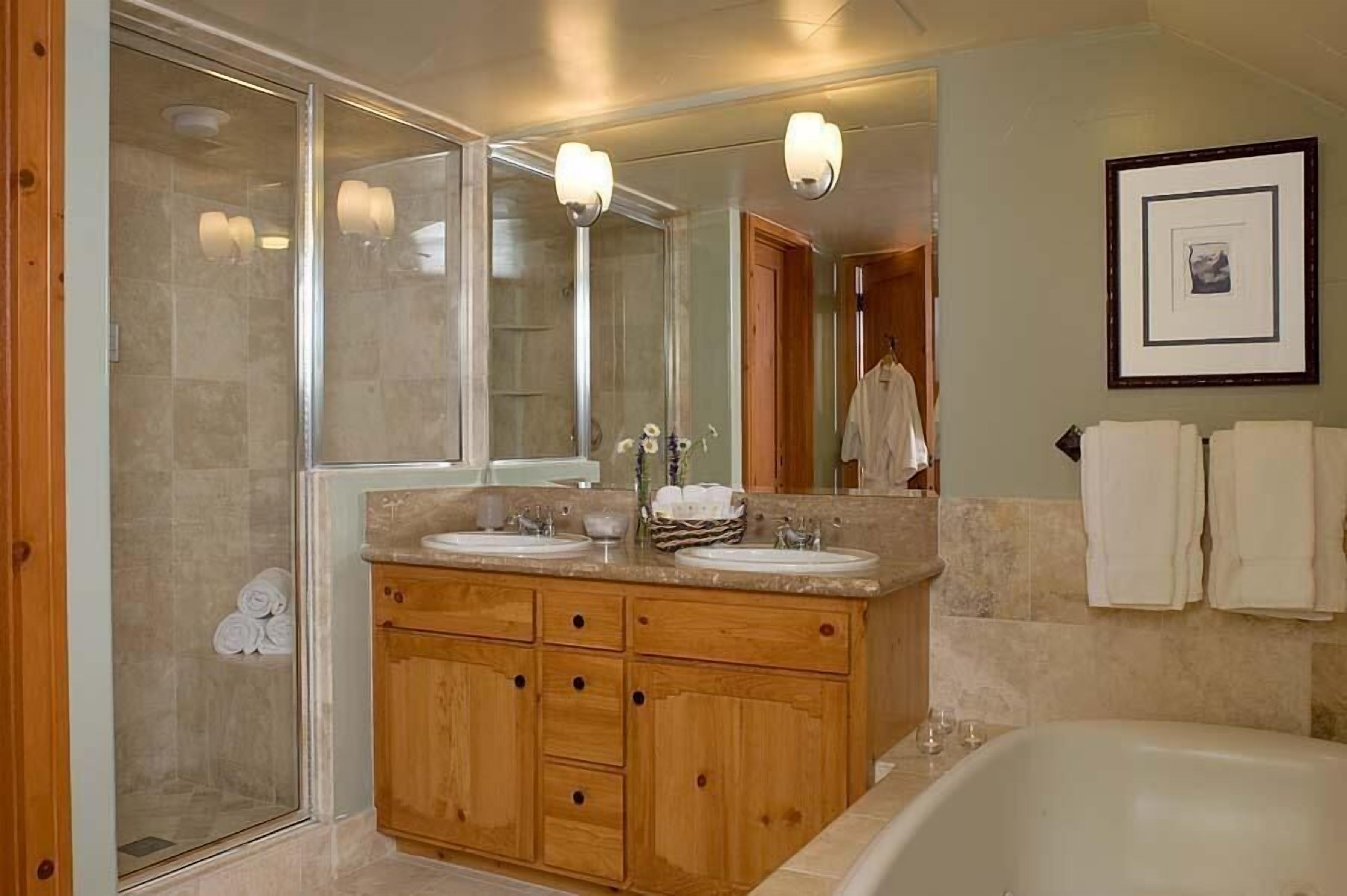 A bathroom with a glass shower enclosure, wooden vanity with two sinks, and a bathtub.
