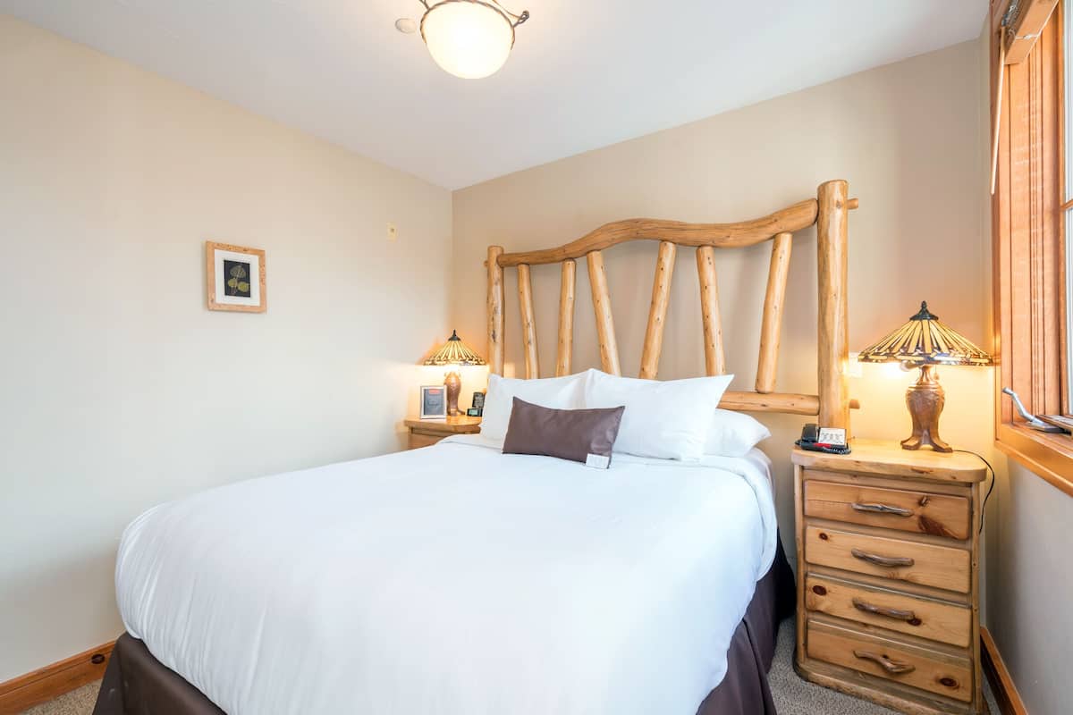 Un lit bien fait, avec du linge de lit blanc, une tête de lit en bois, des lampes de chevet et un petit tableau encadré accroché au mur.