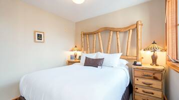 A neatly made bed with white linens, a wooden headboard, bedside lamps, and a small framed picture on the wall.