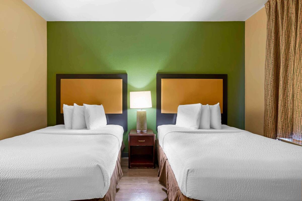 Ein Hotelzimmer mit zwei Betten, einem Nachttisch mit Lampe und einer grünen Wand.