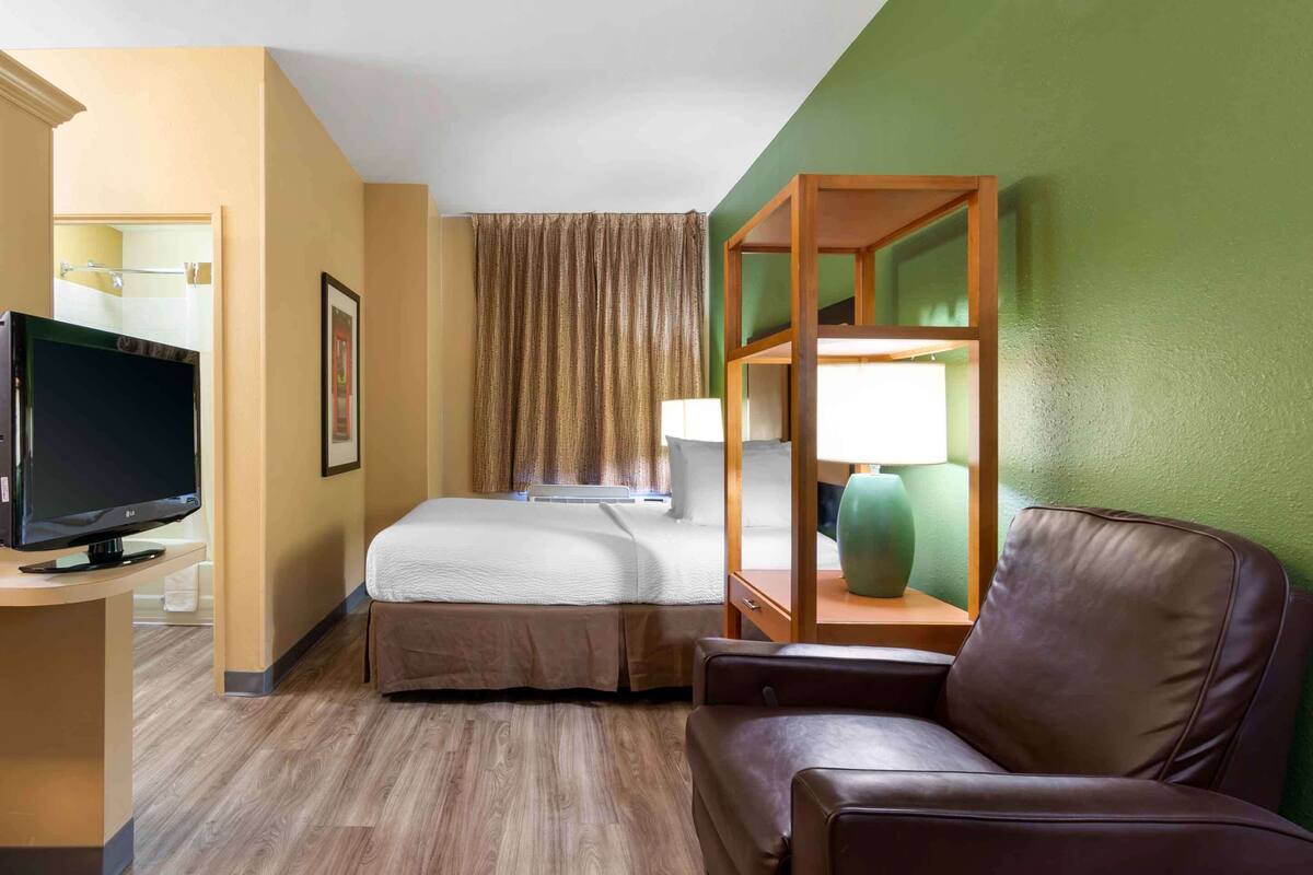 Ein Hotelzimmer mit einem Bett, einem Fernseher, einem Schreibtisch, einem Sessel und einer grünen Wand.
