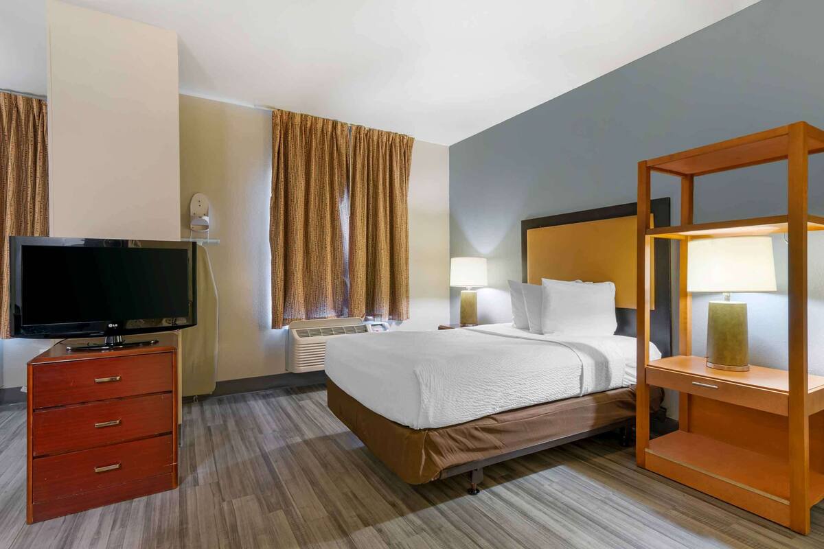 Ein Hotelzimmer mit einem Bett, einem Fernseher, einem Schminktisch, einer Lampe und Vorhängen.