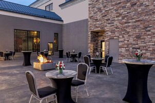 Un patio al aire libre con mesas y sillas redondas, una chimenea y un muro de piedra.