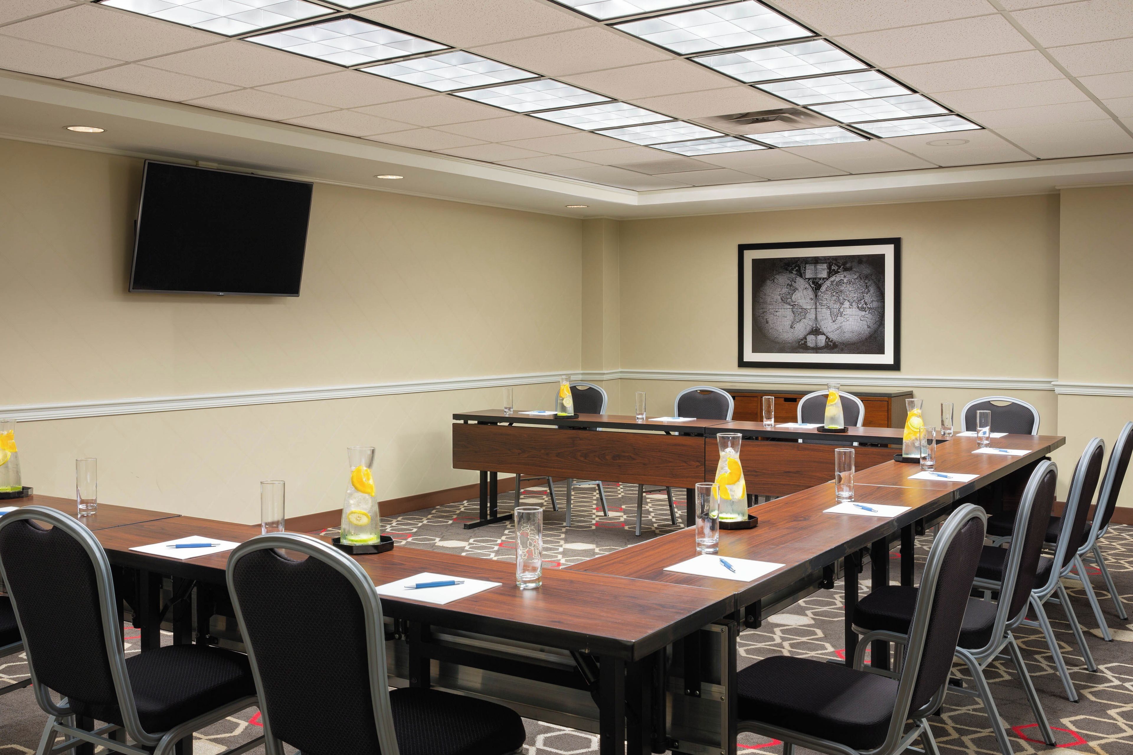 A conference room with a long table, chairs, a projector screen, and a framed map on the wall.