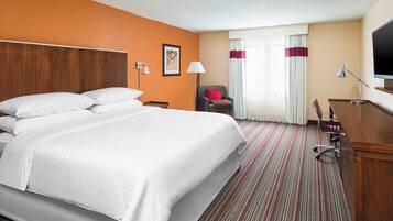 Een hotelkamer met een groot bed, een bureau, een stoel, een televisie en een raam met gordijnen.